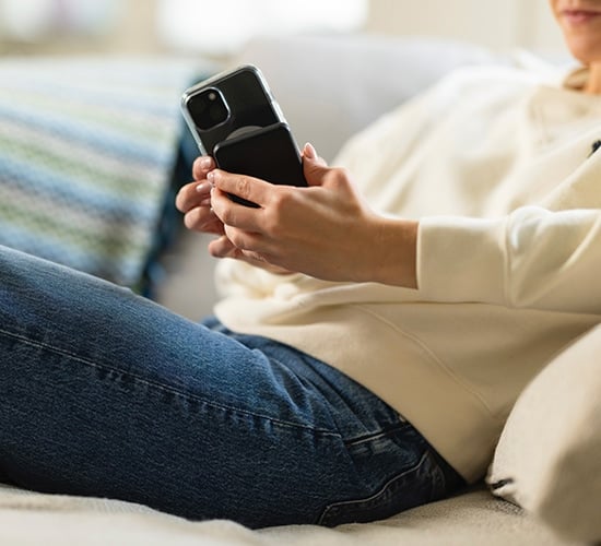 Smartphone med MagSafe-skal och MagSafe-powerbank fäst på baksidan, hålls i handen av person som sitter i soffa i hemmiljö.